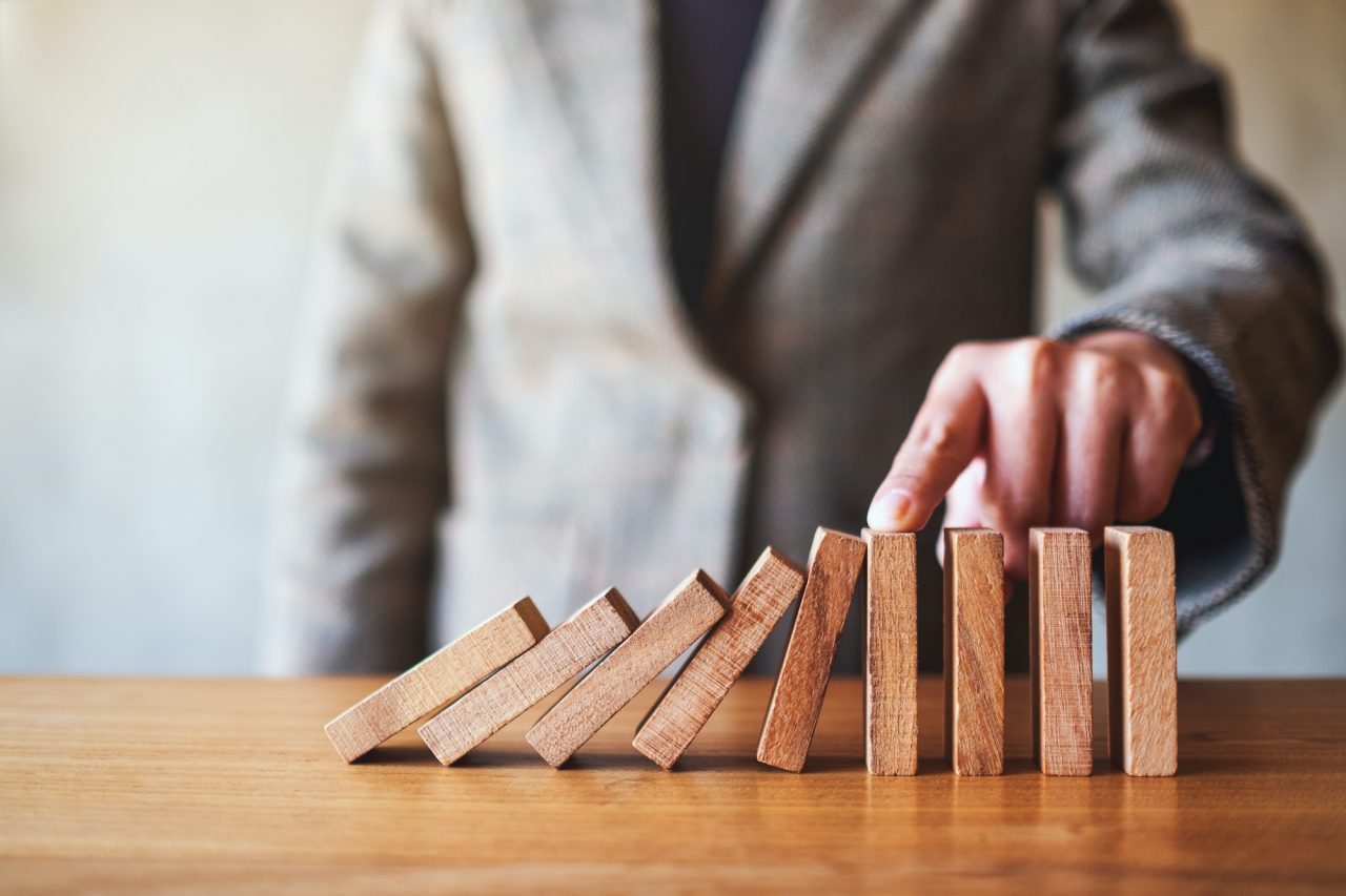 a-businesswoman-s-finger-try-to-stopping-falling-wooden-dominoes-blocks.jpg